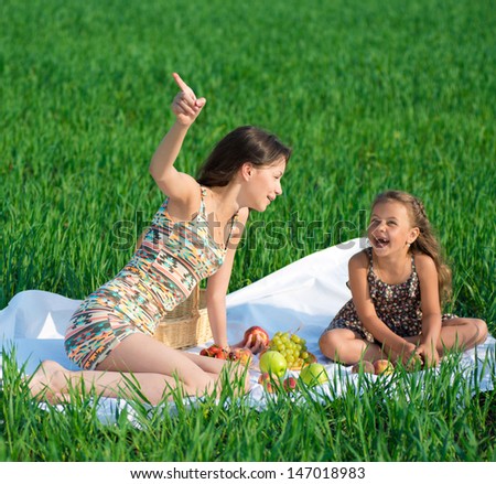 Happy girls on green grass at spring or summer park picnic. One girl point upside
