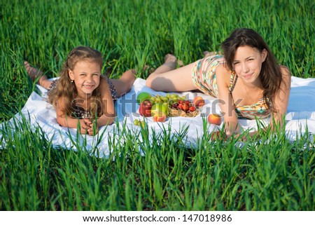 Happy girls on green grass at spring or summer park picnic with fruits