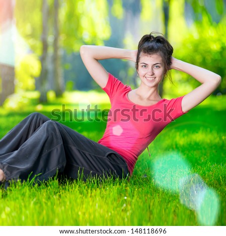 Woman doing strength exercises for abdominal muscles at outdoor sport exercise. Smiling happy doing yoga stretches after running. Fitness model outside in green park  on summer day.