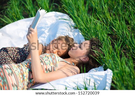 Happy girls reading book on green grass at spring or summer park picnic