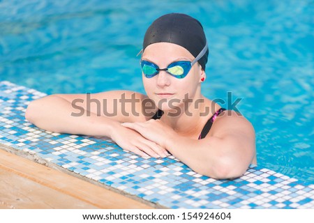 Portrait of a female swimmer wearing a swimming cap and goggles in blue water swimming pool. Sport woman.