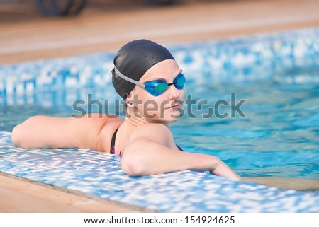 Portrait of a female swimmer wearing a swimming cap and goggles in blue water swimming pool. Sport woman.