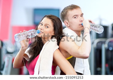 Man and woman drinking water after sport exercises. Fitness gym.