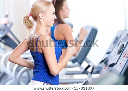 Two Young Sporty Women Run On Machine In The Gym Centre