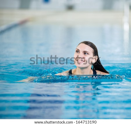 Portrait of a young woman with long hairs in swimming pool. Relaxing after fitness exercises. Indoor sport pool with blue water.