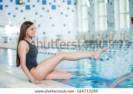 Portrait of a young woman with long hairs near swimming pool. Relaxing after fitness exercises and splashing water. Indoor sport pool with blue water.