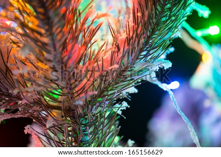 Shining lights of a natural Christmas tree covered snow. New years night black outdoor background. Close Up macro shoot.