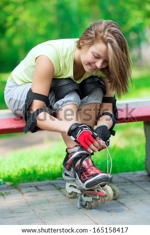 Woman skating in park. Girl going rollerblading sitting on bench  putting on inline skates. Sporty caucasian woman in outdoor fitness activities.