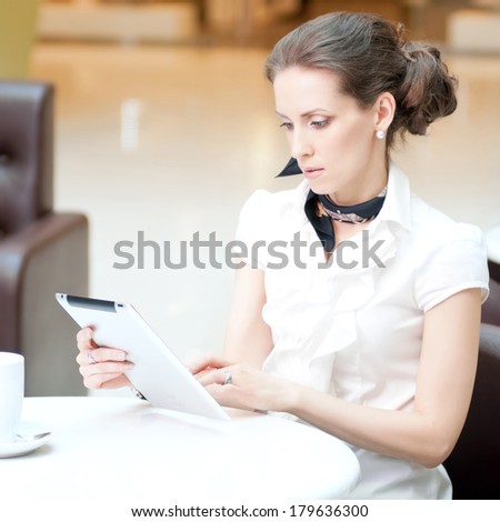 Young professional businesswoman sitting at table at cafe and using tablet on lunch break