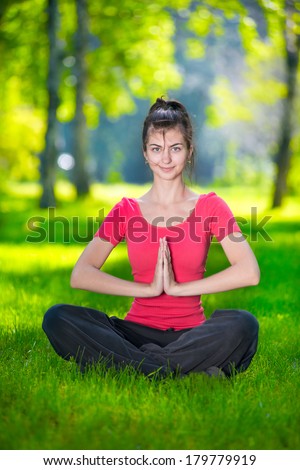 Young woman doing yoga exercises at the summer green city park. In the lotus posture close up