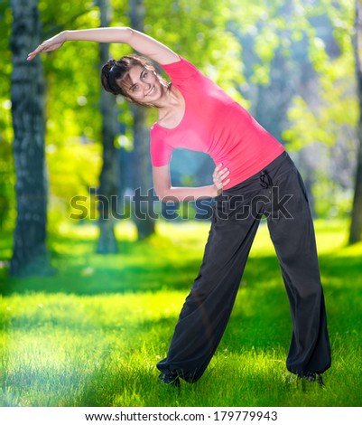 Stretching woman in outdoor sport exercise. Smiling happy doing yoga stretches after running. Fitness model outside in park at summer day.