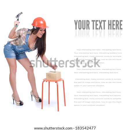 Young emotional woman dressed in jeans and orange helmet hammer in nail in wood piece. Isolated on white.