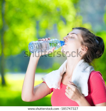 Young woman drinking cold mineral water after sport fitness exercise at green summer park