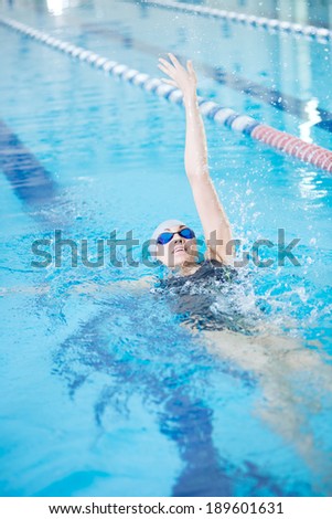 Young woman in goggles and cap swimming back crawl stroke style in the blue water indoor race pool
