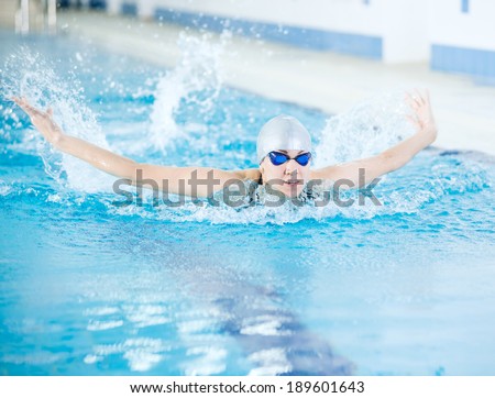 Young woman in goggles and cap swimming butterfly stroke style in the blue water indoor race pool