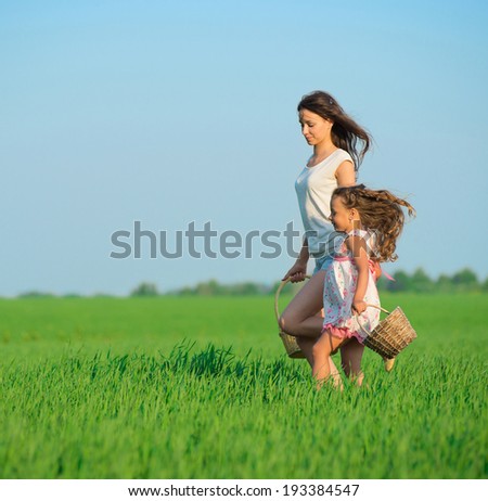 Young happy girls running with basket at green wheat field with her friend together