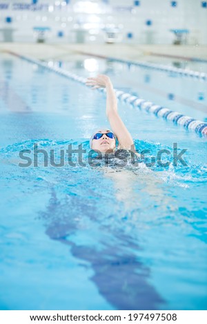 Young woman in goggles and cap swimming back crawl stroke style in the blue water indoor race pool