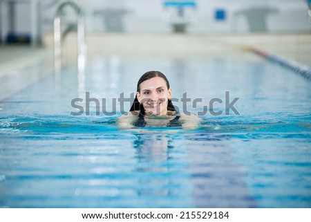 Portrait of a young woman with long hairs in swimming pool. Relaxing after fitness exercises. Indoor sport pool with blue water.