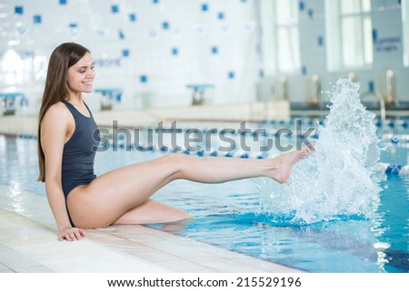 Portrait of a young woman with long hairs near swimming pool. Relaxing after fitness exercises and splashing water. Indoor sport pool with blue water.