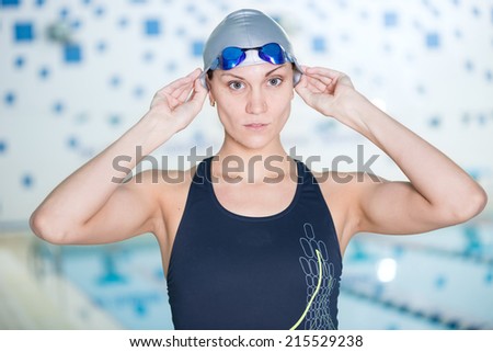 Portrait of a female swimmer, that wearing a swimming cap and goggles and preparing to jump into swimming pool. Sporty woman.
