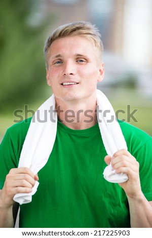 Tired man with white towel after fitness time and exercising in city street park at beautiful summer day. Sporty model caucasian ethnicity training outdoor.