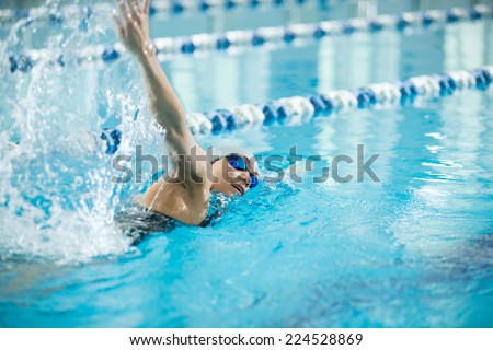 Young woman in goggles and cap swimming front crawl stroke style in the blue water indoor race pool