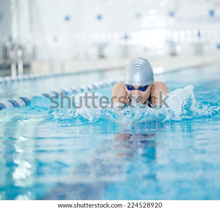 Young woman in goggles and cap swimming breaststroke stroke style in the blue water indoor race pool