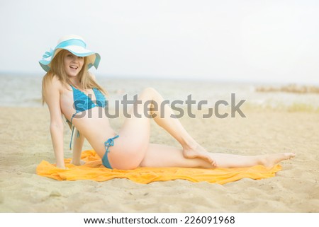 Young lady sunbathing on a beach. Beautiful woman posing at the summer sand beach. Outdoor summer portrait of pretty sport style woman in blue bikini. Sexy slim model caucasian ethnicity outdoors.