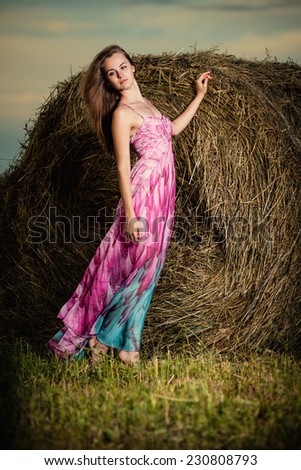 Beautiful woman posing at the old rural farm location. Outdoor summer portrait of pretty fashion style woman in colored dress over haystack.  Sexy slim model caucasian ethnicity outdoors.