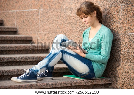 Preparing to exams outdoors. Beautiful young female student writing or reading something from note pad.  Woman sitting on stairs in city park.