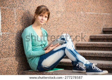 Preparing to exams outdoors. Beautiful young female student writing or reading something from note pad.  Woman sitting on stairs in city park.
