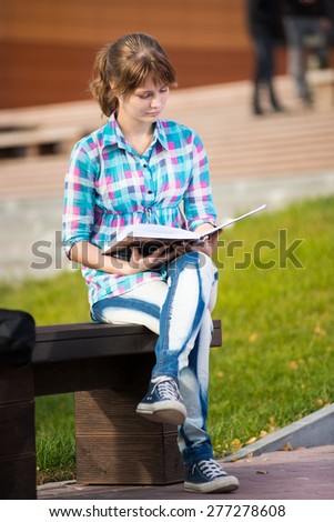 Student girl with copybook on bench outdoor. Summer campus park. Studying to exam.