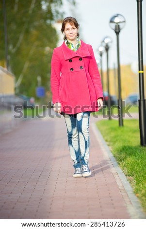 Beautiful woman in red coat walking autumn street. Girl walking on a beautiful fall day.