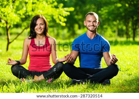 Young man and woman doing yoga in the sunny summer park. Couples Yoga on green grass outdoor.