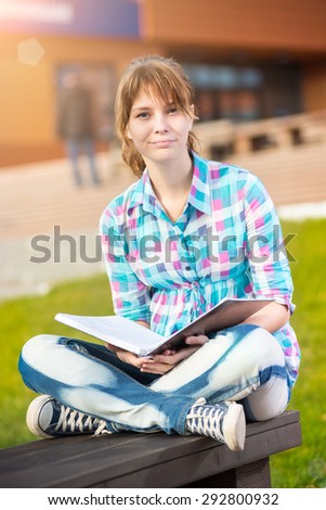 Student girl with copybook on bench outdoor. Summer campus park. Studying to exam.