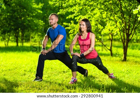 Man and woman doing stretching exercises at summer park.  Young couple exercising and stretching muscles before sport activity - outdoor in nature