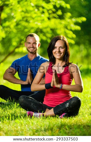 Young man and woman doing yoga in the sunny summer park. Couples Yoga on green grass outdoor.
