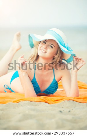 Young lady sunbathing on a beach. Beautiful woman posing at the summer sand beach. Outdoor summer portrait of pretty sport style woman in blue bikini. Ocean sea coast. Beautiful fit tan girl. Sexy