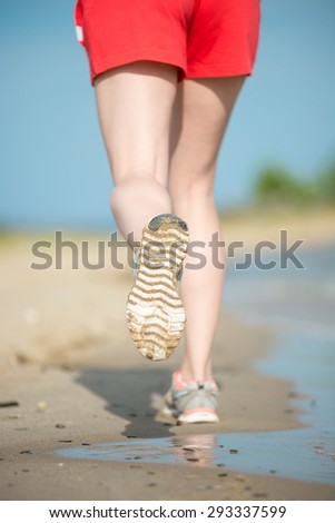 Sport footwear, sand footprints and legs close up. Runner feet detail. Workout near ocean sea coast. Beautiful fit girl. Fitness model caucasian ethnicity outdoors. Weight loss exercise. Jogging.