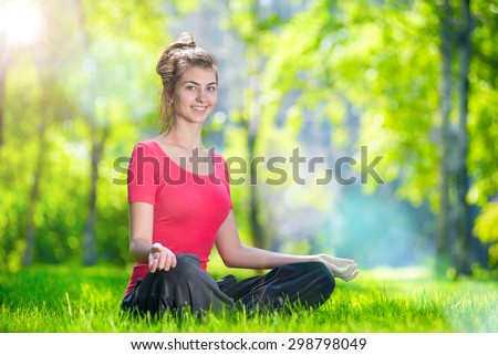 Young woman doing yoga exercises at the summer green city park. In the lotus posture close up