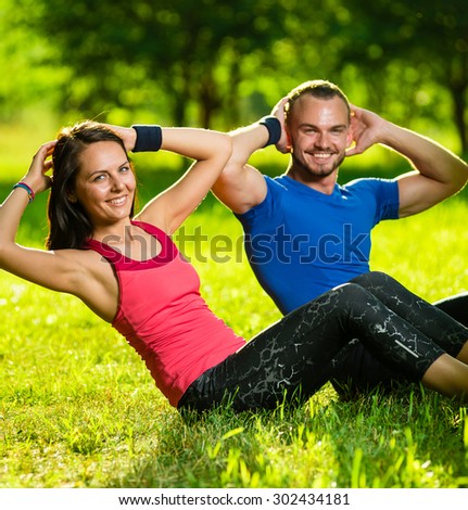 Man and woman exercising at the city park. Beautiful young multiracial couple. Sit ups fitness couple exercising outside in grass. Fit happy people working out outdoor.