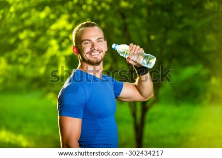 Athletic sport man drinking water from a bottle. Cold drink after outdoor fitness.