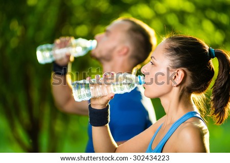 Man and woman drinking water from bottle after fitness sport exercise. Smiling couple with bottles of cold drink outdoors