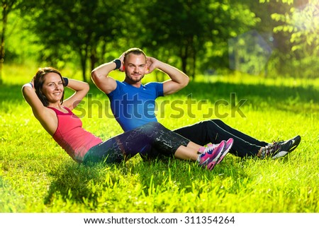 Man and woman exercising at the city park. Beautiful young multiracial couple. Sit ups fitness couple exercising outside in grass. Fit happy people working out outdoor.