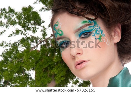 Close-up portrait of beautiful sprite girl with green faceart on white posing with plant