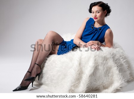 Beautiful glamour woman in blue dress on white fur sofa