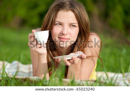 Beautiful young woman drink hot coffee outdoor on green grass
