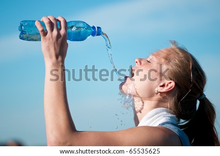 Beautiful young woman drinking water after exercise on sunny summer day