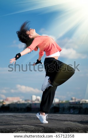Beautiful woman dancing hip-hop modern style over urban city landscape, blue sky and sun