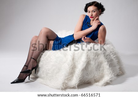 Beautiful glamour woman in blue dress on white fur sofa